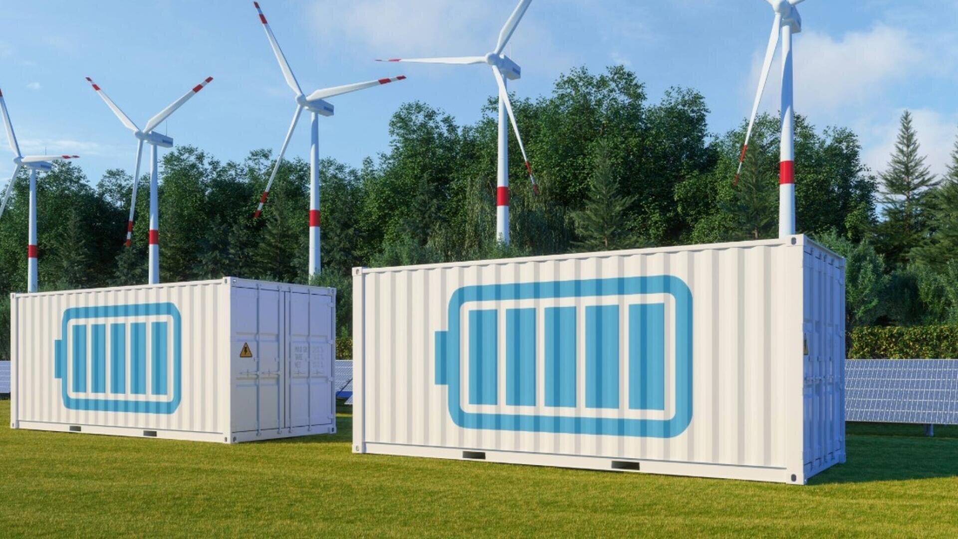Weiße Schiffscontainer mit großen Batteriesymbolen stehen auf einer Wiese, mit Windturbinen und Solarzellen im Hintergrund, in der Nähe einer Reihe von grünen Bäumen unter blauem Himmel.