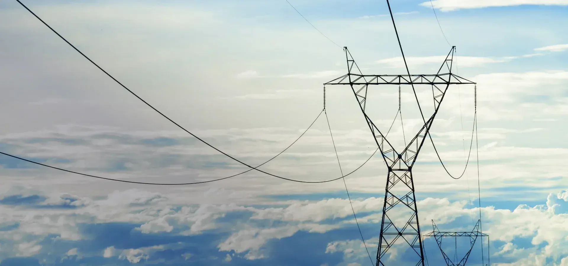 Tall metal electricity pylons and power lines stretch across the sky, with clouds and soft sunlight creating a serene backdrop.