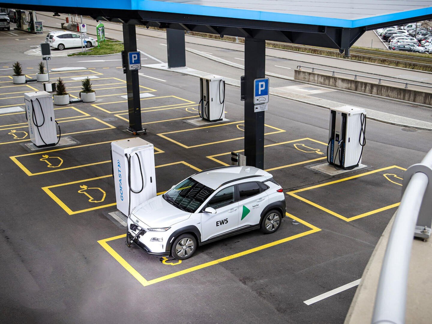 A white electric car parked in a modern parking lot at a charging station for electric vehicles, surrounded by several empty charging stations and chargers.