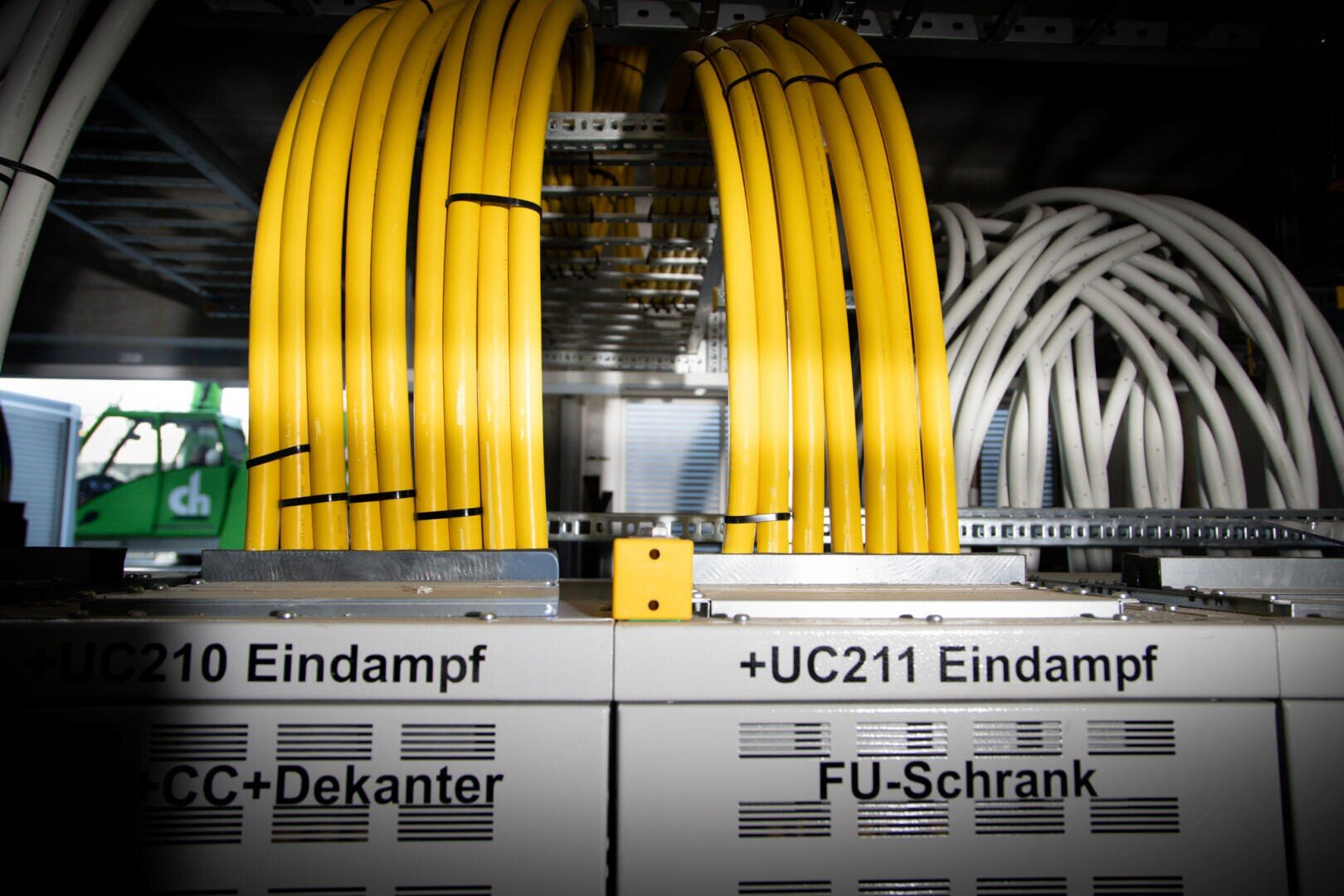 Yellow and white network cables are arranged and connected to labeled server cabinets with labels such as +UC210 Vaporization and +UC211 Vaporization on their metal surfaces.