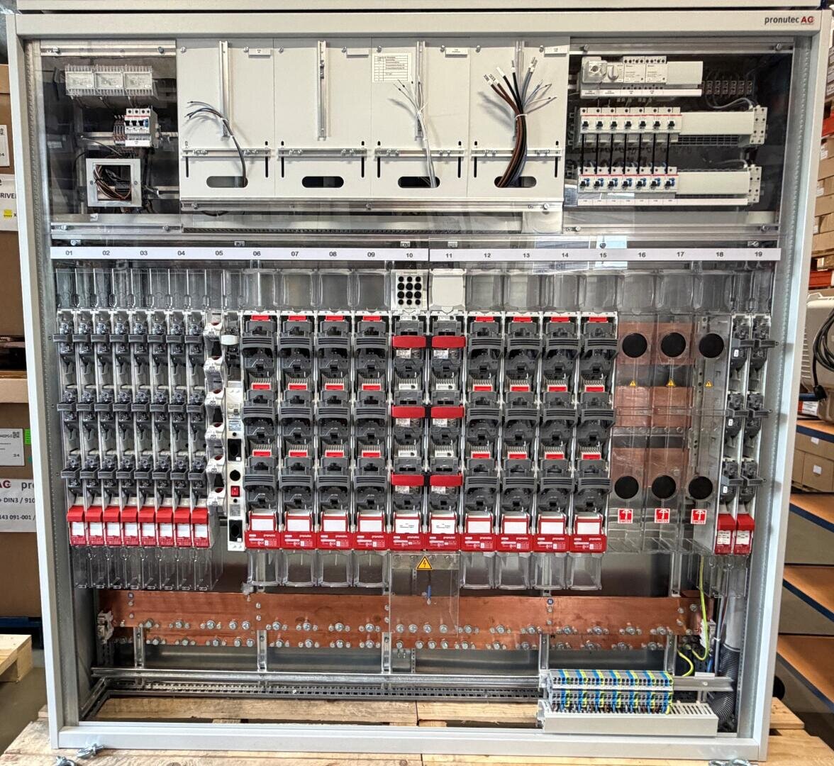 Industrial electrical switch panel with several circuit breakers, relays, fuses, wiring terminals and labeled modules, which are clearly arranged in a metal housing. Some wires are not yet connected.