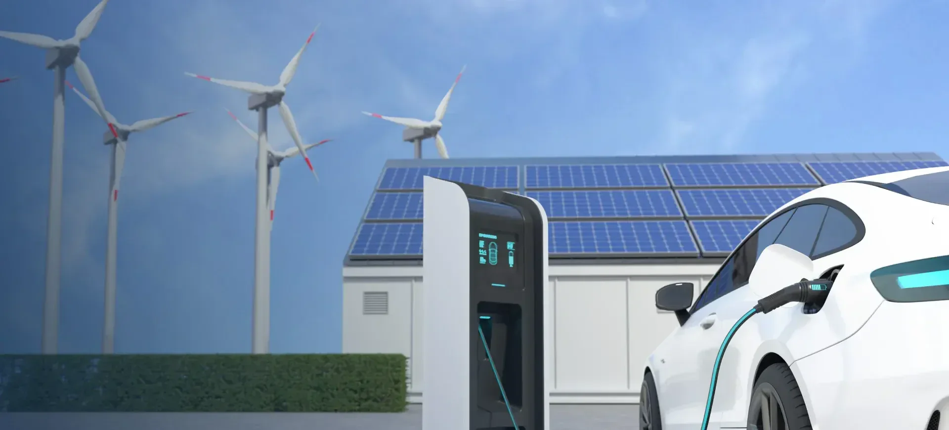 Ein weißes Elektroauto lädt sich an einer Station vor einem Gebäude mit Solarpaneelen auf dem Dach auf, während im Hintergrund unter blauem Himmel mehrere Windkraftanlagen zu sehen sind.