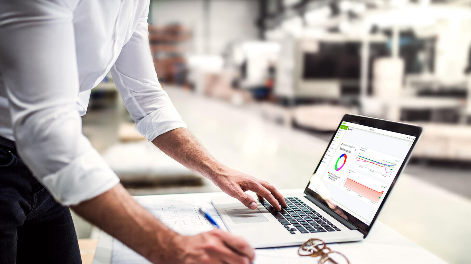 A person working on a laptop displaying energy and consumption analysis. The illustration shows the use of digital tools for energy data management, analysis, and monitoring in industrial applications.