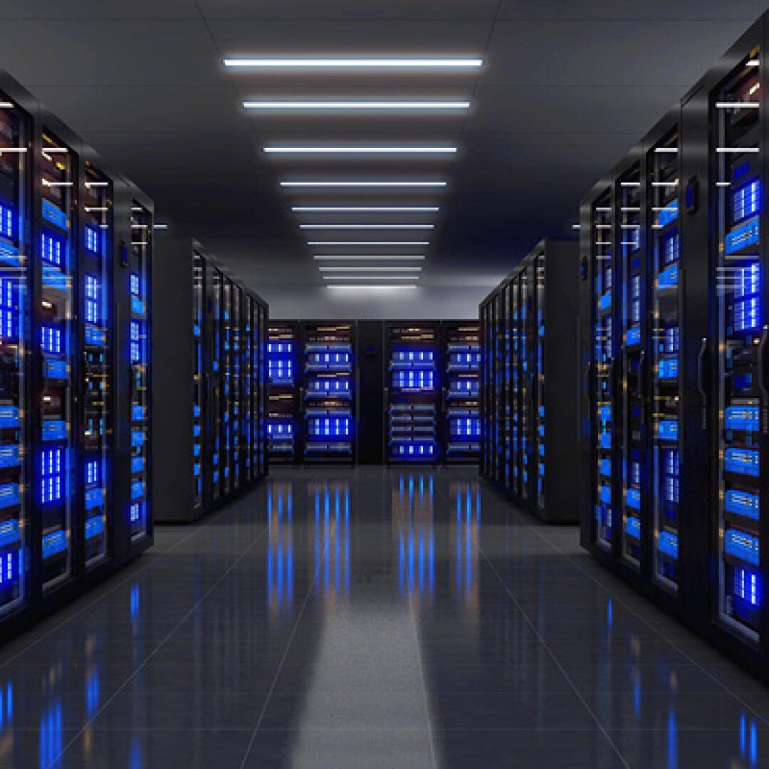 Ein modernes Rechenzentrum mit Reihen schwarzer Serverschränke, die jeweils mit blau leuchtenden Geräten bestückt sind. Der glänzende Boden spiegelt die Racks und die Lichtbänder über den Köpfen wider und schafft eine saubere, hochtechnologische Umgebung.
