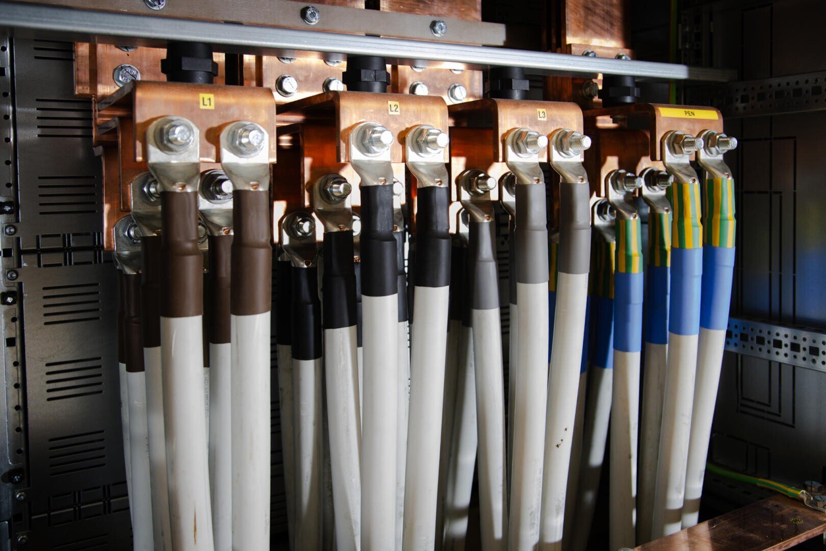 Close-up of several thick electrical cables connected to copper rails in a control panel, with each cable color-coded and labeled, representing a power distribution system.
